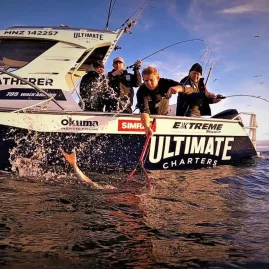 Group of anglers landing a fish beside Ultimate Charters Gatherer boat in the Gulf