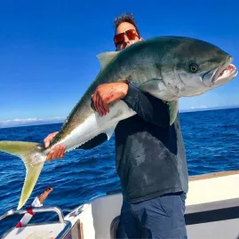 Angler holding a giant kingfish on a clear day off the Auckland coast