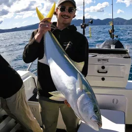 Young man holding a freshly caught kingfish on Ultimate Charters trip