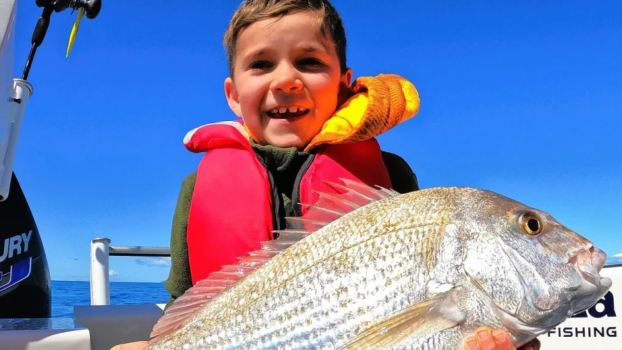 Young boy smiling while holding a snapper on Ultimate Charters boat