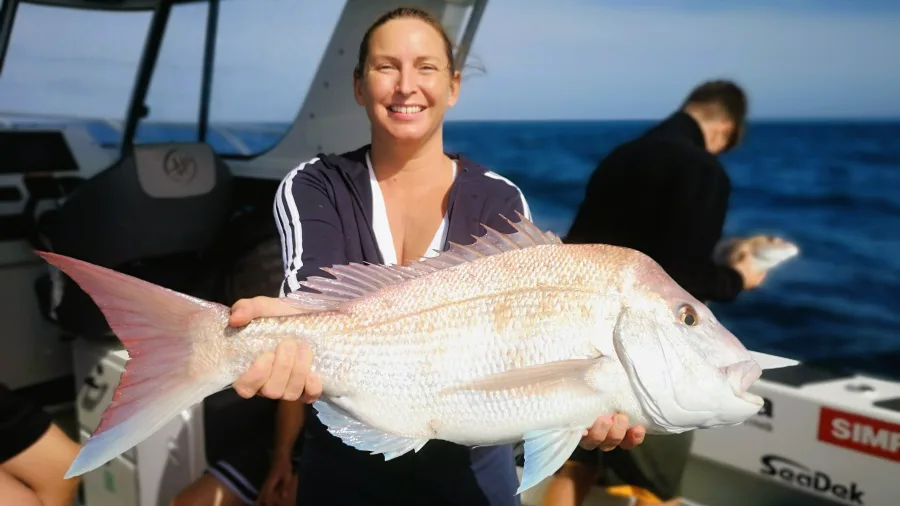 Woman holding a large snapper aboard an Ultimate Charters fishing boat