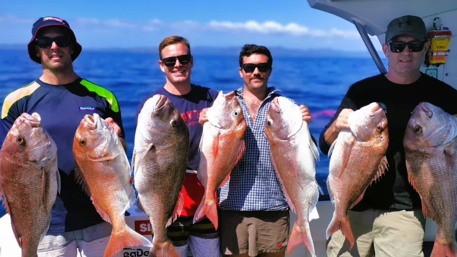 Four anglers showing off snapper catch with blue ocean in background