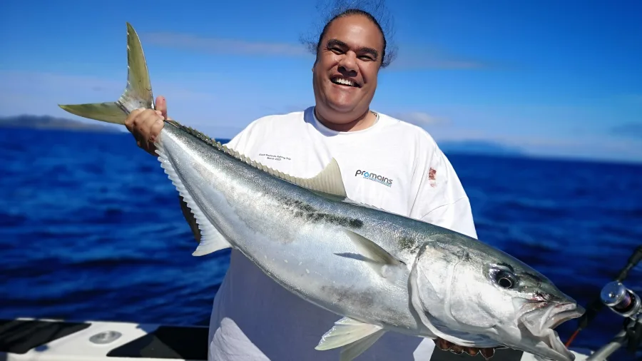 Angler smiling and holding kingfish on board Ultimate Charters boat
