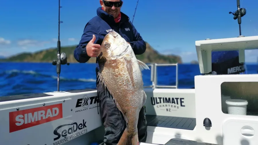 Fisherman giving thumbs up holding a large snapper on charter boat