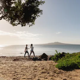 Women walking on beach with Rangitoto Island view
