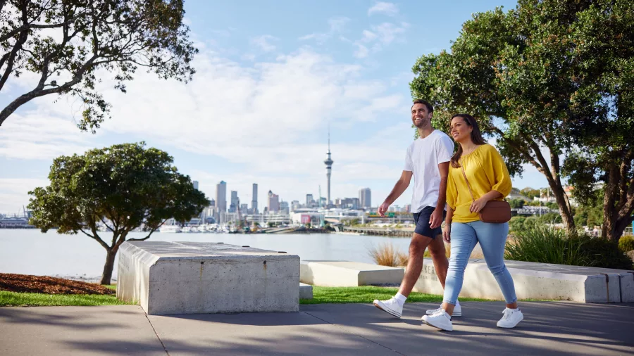 Couple walking with Westhaven Marina and Auckland City skyline in the background