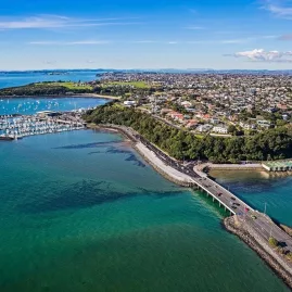Aerial view of Tamaki Drive in Auckland, showing the waterfront, marina, and surrounding cityscape on a sunny day.