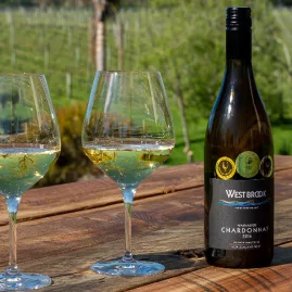 Bottle of West Brook Chardonnay with two glasses on vineyard deck