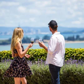A glass of wine elegantly poured at Mudbrick Vineyard, overlooking scenic coastal views and manicured gardens.