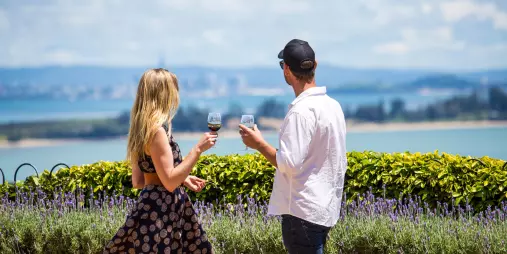 A glass of wine elegantly poured at Mudbrick Vineyard, overlooking scenic coastal views and manicured gardens.