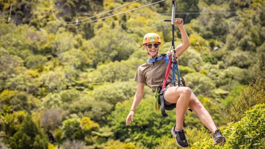 Person ziplining with arms outstretched over the native forest at EcoZip Waiheke, enjoying an aerial adventure in wine country