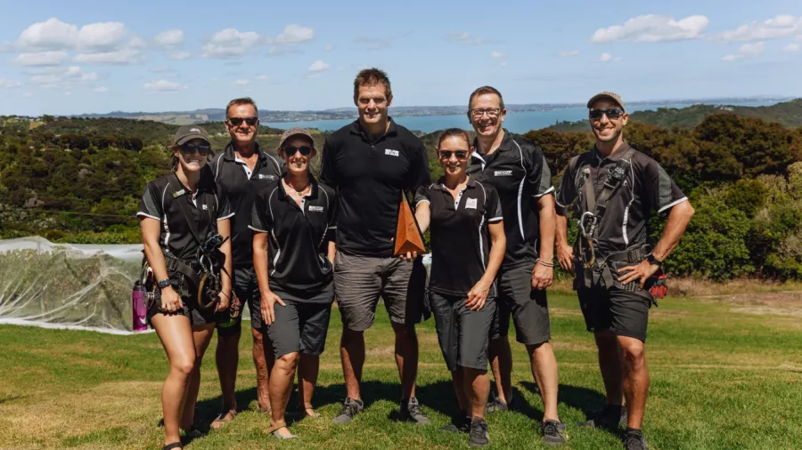EcoZip Waiheke team standing together outdoors in gear, ready for adventure with forested hills and vineyards in the background