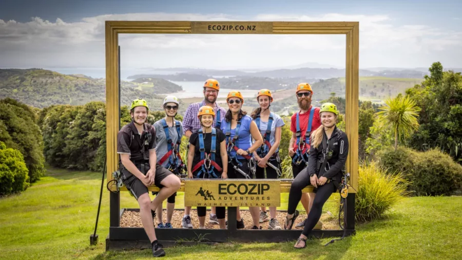 Group in zipline harnesses posing at EcoZip Waiheke with scenic island views in the background