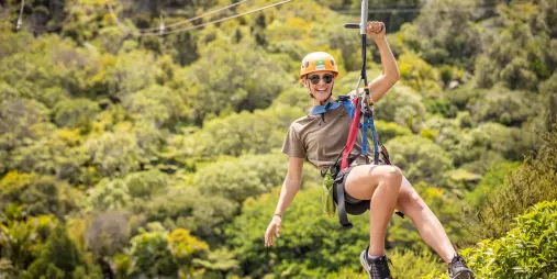 Person ziplining with arms outstretched over the native forest at EcoZip Waiheke, enjoying an aerial adventure in wine country