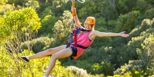 Person ziplining with arms outstretched above the native forest at EcoZip Waiheke Island, enjoying an eco adventure tour