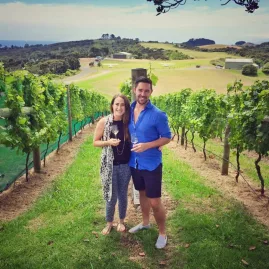 Couple standing among rows of grapevines enjoying a wine tasting experience on Waiheke Island’s Premium Wine Tour