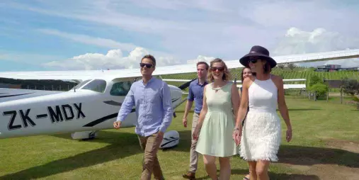 Group of people walking on grass beside a Waiheke Wings light aircraft at Waiheke Island Aerodrome, preparing for a scenic flight as part of the Sea, Land & Sky tour with panoramic vineyard and coastal views
