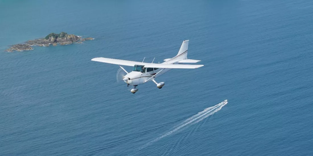 Light aircraft flying over the Hauraki Gulf near Waiheke Island on a scenic flight from Auckland, with a boat visible below.