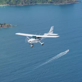 Light aircraft flying over the Hauraki Gulf near Waiheke Island on a scenic flight from Auckland, with a boat visible below.