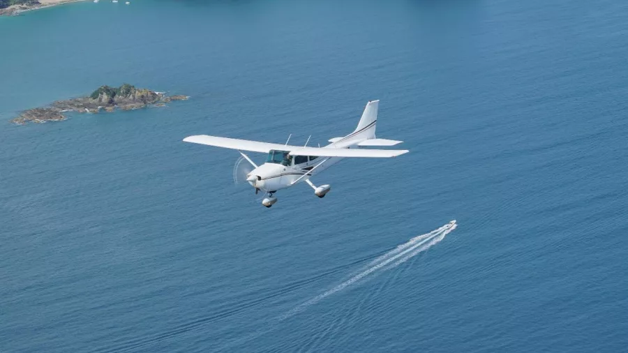 Light aircraft flying over the Hauraki Gulf near Waiheke Island on a scenic flight from Auckland, with a boat visible below.