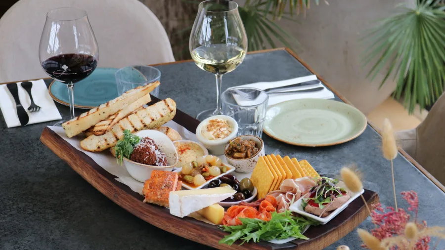 Gourmet lunch and wine tasting platter served at a Waiheke Island vineyard restaurant, featuring artisan breads, cheeses, charcuterie, and wine glasses as part of a premium Island Aviation tour