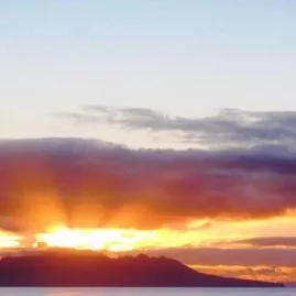 Golden sunset casting warm light over Little Barrier Island coastline