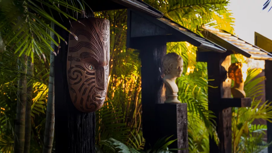 Maori-inspired carved mask and classical bust sculpture displayed in lush tropical garden at Sculptureum Matakana New Zealand