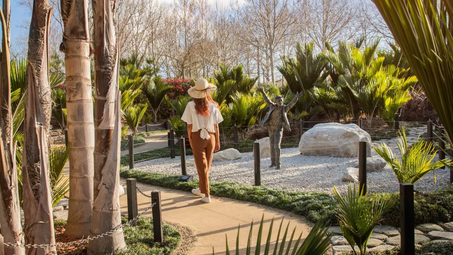 Young girl exploring winding garden path surrounded by sculptures and palms at Sculptureum Matakana
