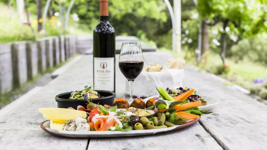Gourmet platter and Brick Bay red wine at a rustic vineyard table in Snells Beach surrounded by vines