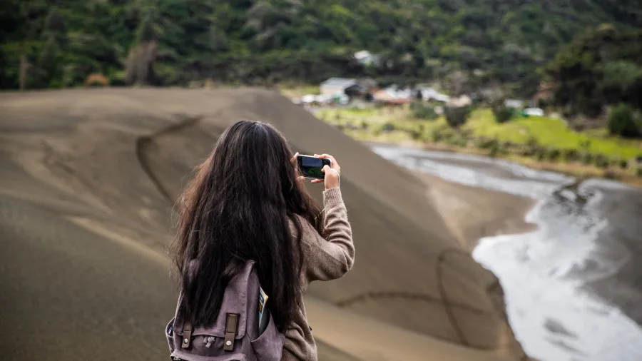 Girl taking photo at Bethells Beach sand dunes Auckland