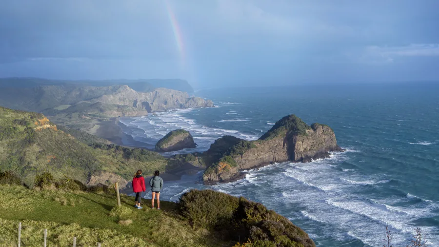 Hikers at Te Henga Bethells Beach Auckland west coast cliff with rainbow