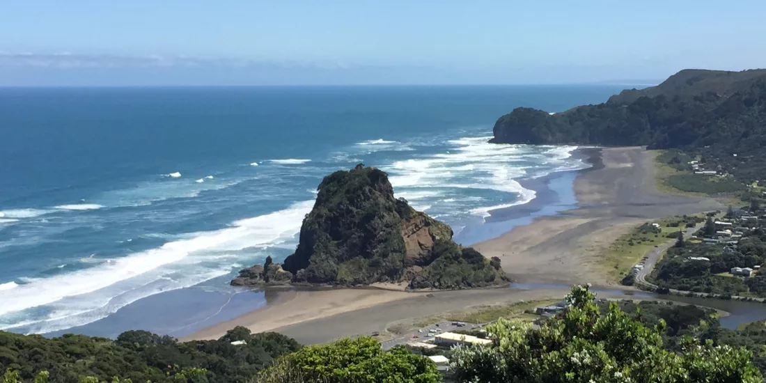 Rugged Piha coastline with black sand beach, sea cliffs, and crashing Tasman Sea waves on New Zealand’s west coast