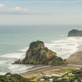 View of Lion Rock at Piha Beach with waves and black sand coastline