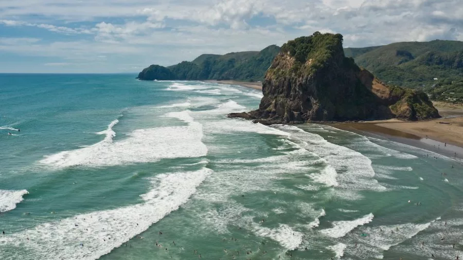 Lion Rock rising from Piha Beach with black sand and surf on New Zealand’s wild west coast