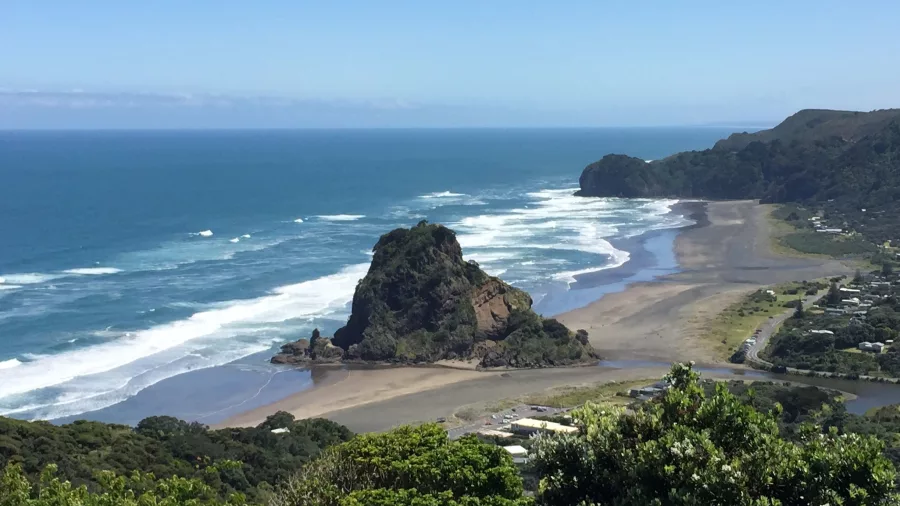 Rugged Piha coastline with black sand beach, sea cliffs, and crashing Tasman Sea waves on New Zealand’s west coast