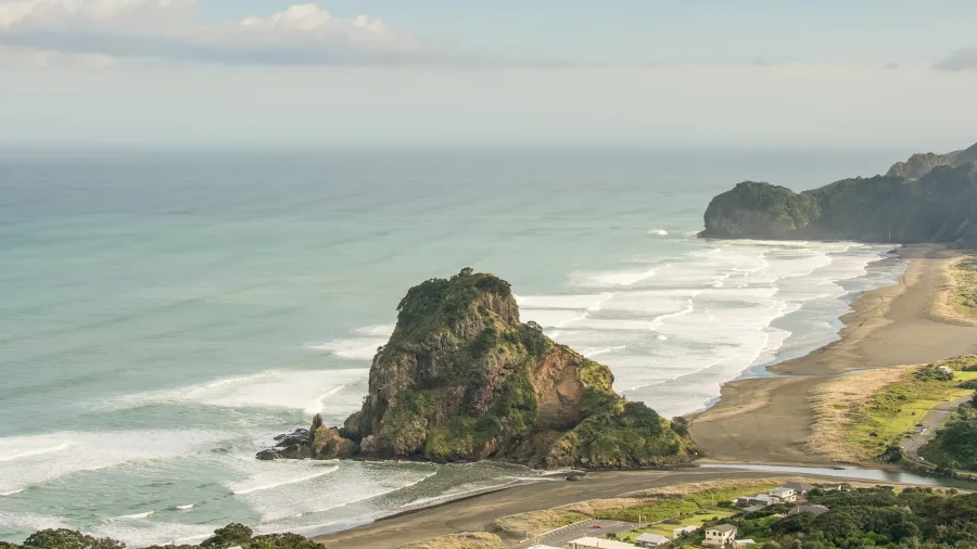 View of Lion Rock at Piha Beach with waves and black sand coastline