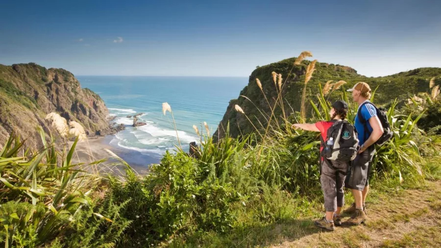Two hikers overlooking the dramatic cliffs and ocean views of Piha Beach from the Mercer Bay Loop Track on Auckland’s West Coast