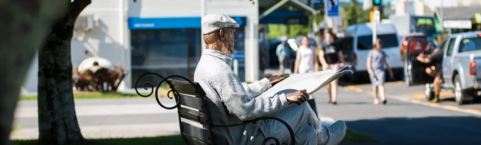 Bronze statue of a man reading a newspaper with a dog at his feet in Katikati town centre, New Zealand