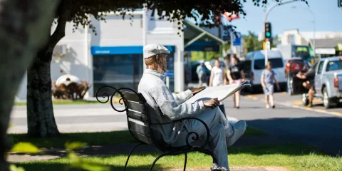 Bronze statue of a man reading a newspaper with a dog at his feet in Katikati town centre, New Zealand