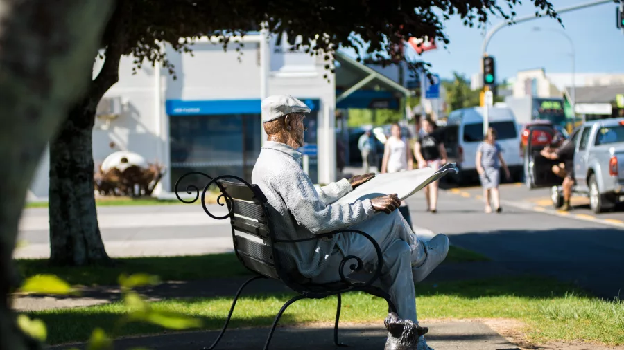 Bronze statue of a man reading a newspaper with a dog at his feet in Katikati town centre, New Zealand