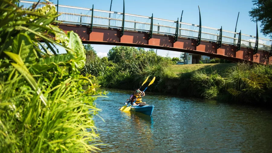 Two people kayaking on the Uretara Stream beneath the Haiku Pathway bridge in Katikati