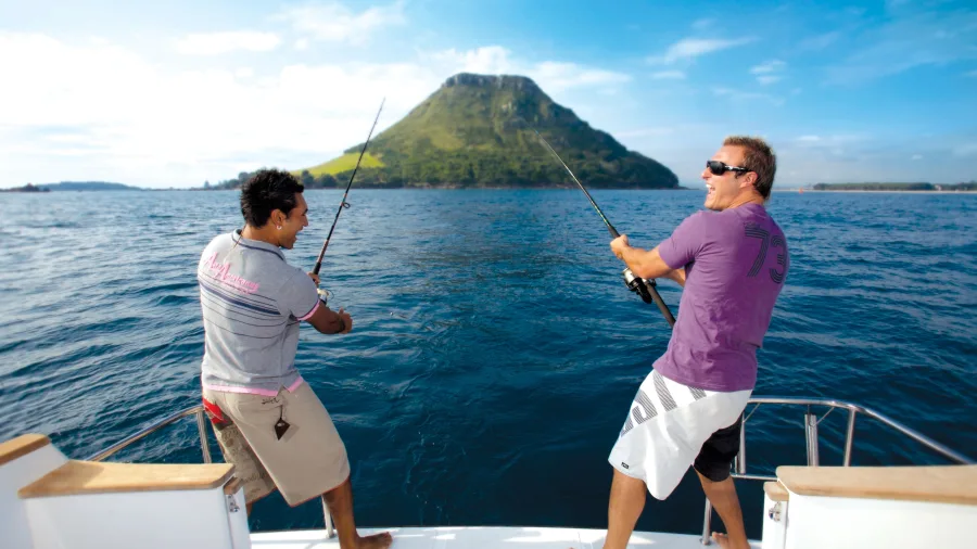 Two friends deep fishing from a boat with Mount Maunganui in the background, Bay of Plenty, New Zealand