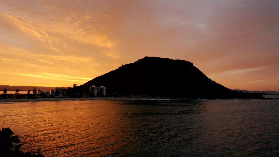 Sunset over Mount Maunganui, Bay of Plenty, New Zealand, with golden skies reflecting on the water
