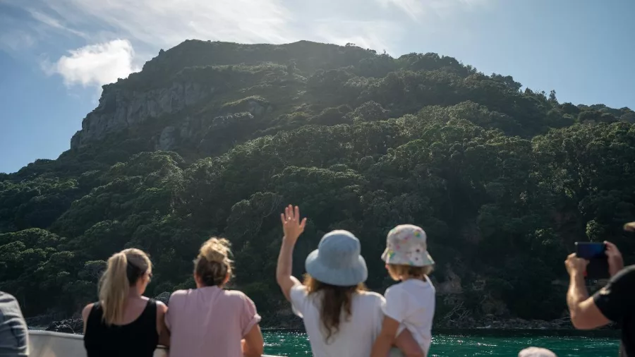 Family waving from the boat while cruising past Mount Maunganui cliffs