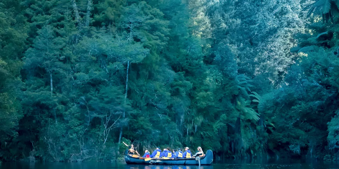Group in a Big Kanu floating on still waters of Lake McLaren beneath dense forest