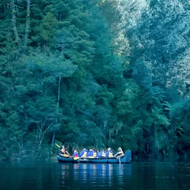 Group in a Big Kanu floating on still waters of Lake McLaren beneath dense forest