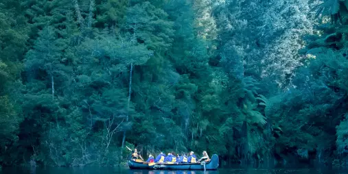 Group in a Big Kanu floating on still waters of Lake McLaren beneath dense forest