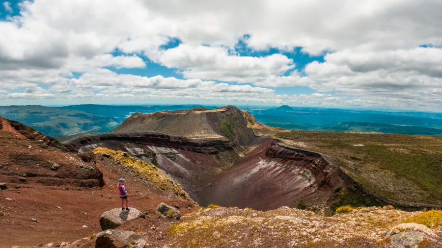 Hiker overlooking the volcanic crater of Mount Tarawera with distant mountain views, Rotorua, New Zealand
