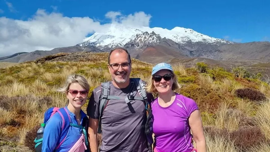Three hikers smiling with Mount Ruapehu behind them on the Taranaki Falls Track