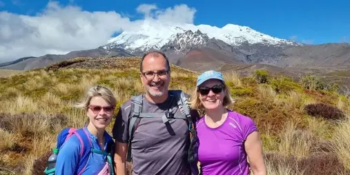Three hikers smiling with Mount Ruapehu behind them on the Taranaki Falls Track